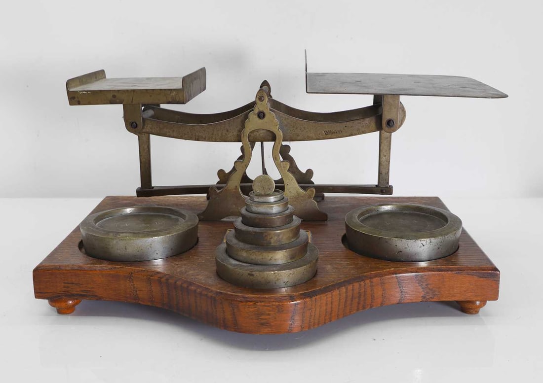 A pair of Victorian postal parcel scales, Circa 1900,: A pair of Victorian postal parcel scales, Circa 1900, of a larger size, with nine weights, centred with an ivorine label, with remnants 'Inland Parcel Post', on a shaped oak plinth 37cm wide, 29cm