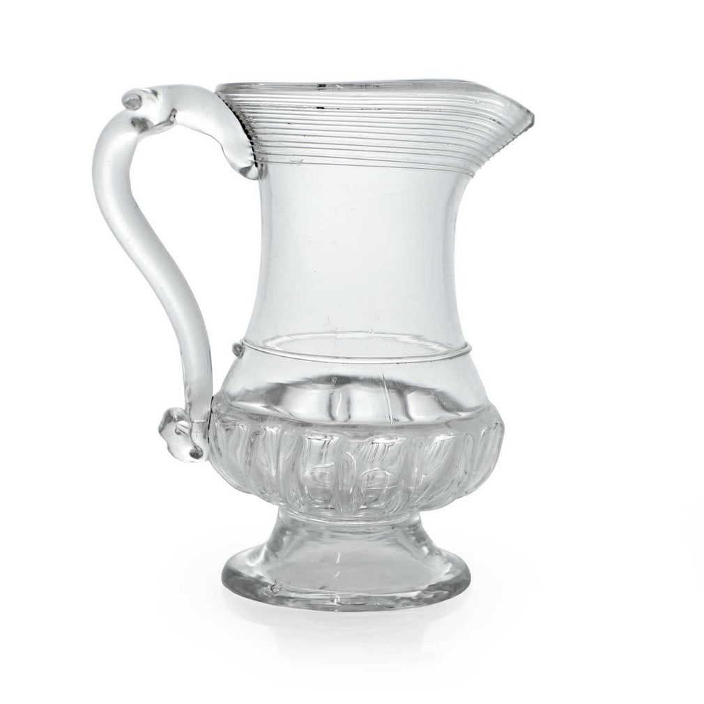 A glass coin jug, circa 1770,: A glass coin jug, circa 1770, of baluster form with a gadrooned base and threaded decoration, with an applied loop handle, the base inset with a George III 1762 threepence (9.5cm wide, 6.6cm deep, 11.