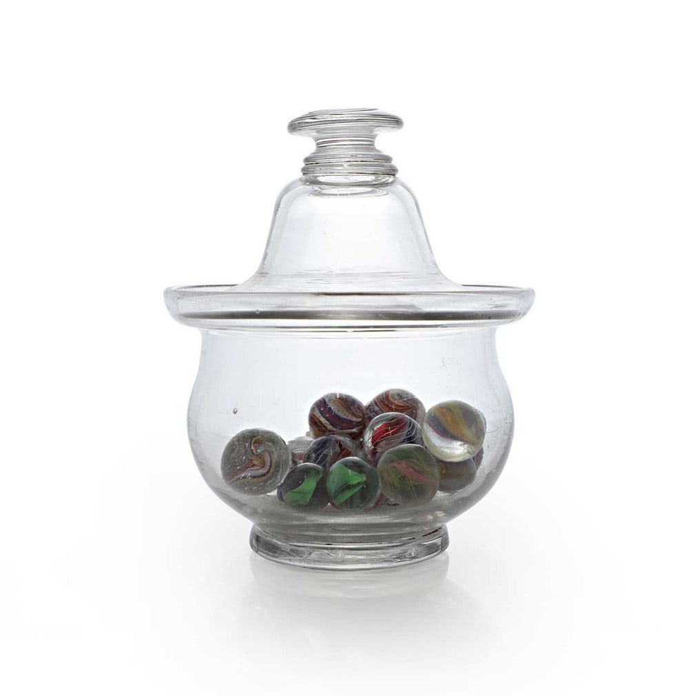 A glass sugar bowl and cover, 19th century,: A glass sugar bowl and cover, 19th century, containing a quantity of Victorian and later marbles (sugar bowl 14.7cm high) (qty.)