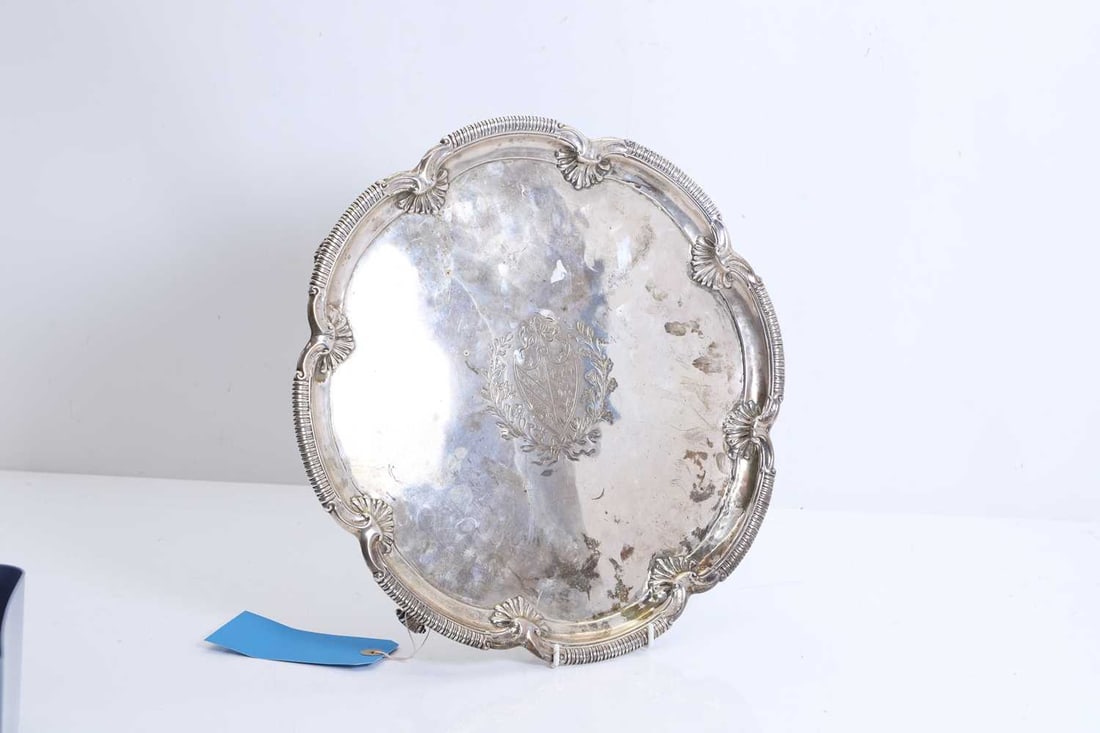 A large silver salver,: A large silver salver, London, 1762, with armorial crest in the central field, encased in a banded and a shell motif border, raised on scrolled feet 37cm diameter, 4.5cm high, 42ozt
