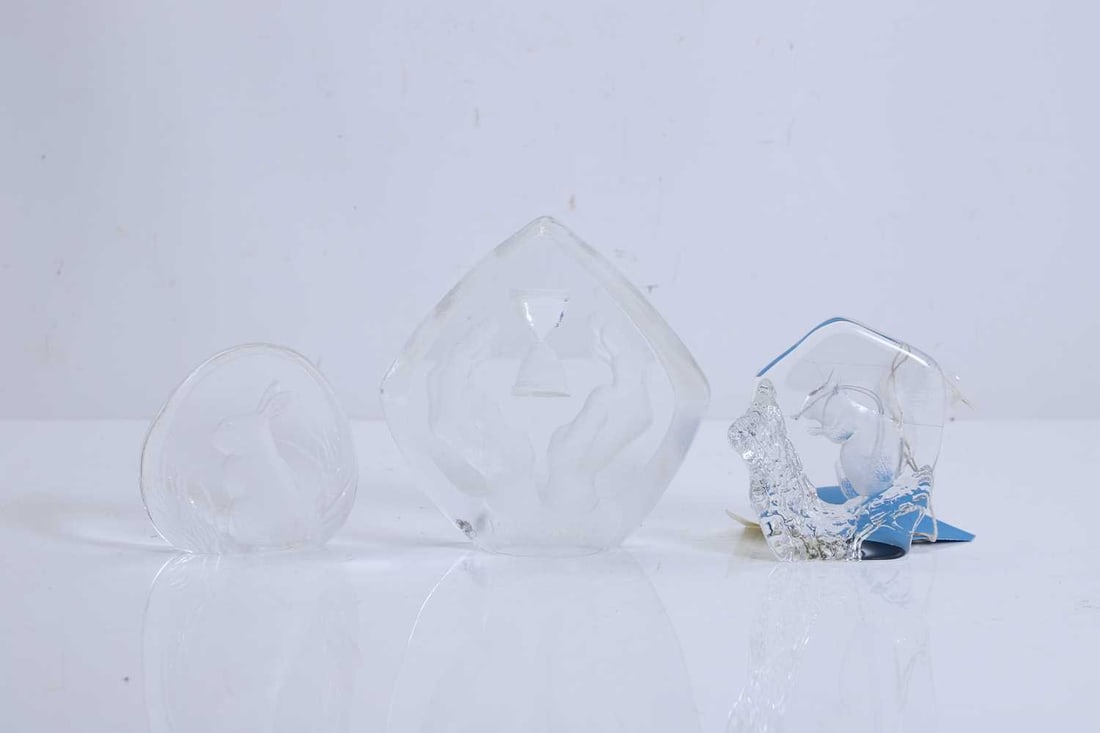 A Mats Jonasson Carpe Diem glass sculpture,: A Mats Jonasson Carpe Diem glass sculpture, design as two hands around an hourglass, labelled 2000, and two similar with squirrel and rabbit detail The largest, 15cm wide, 15cm high 3