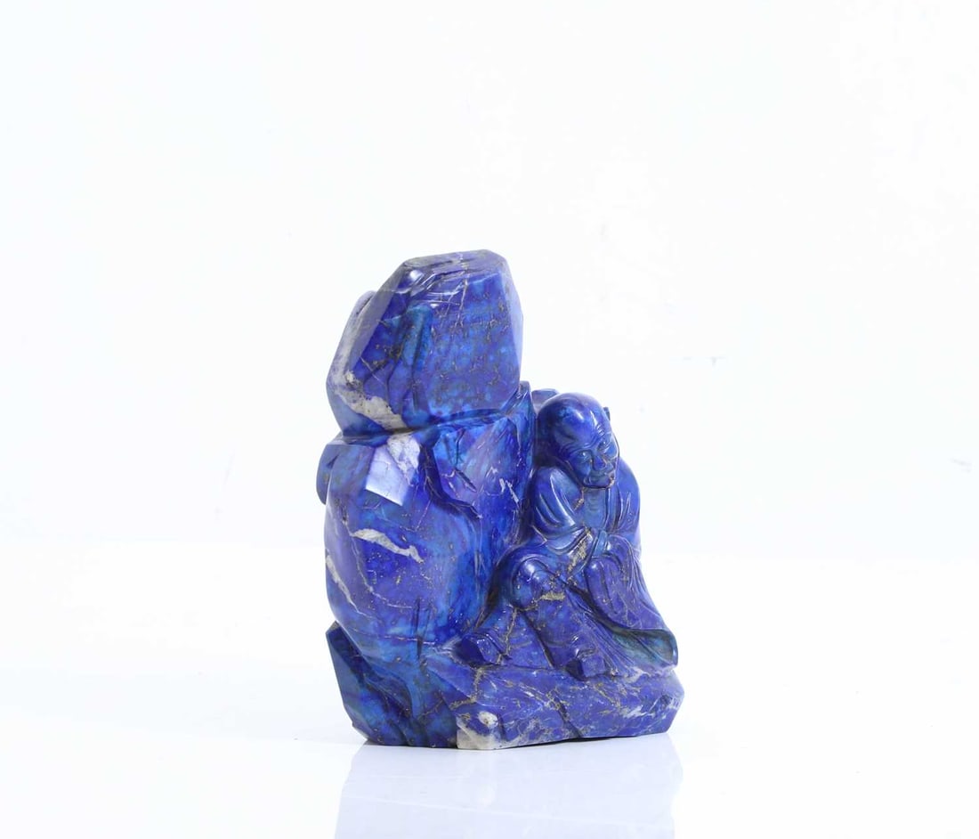 A Chinese carved lapis lazuli figural group, 20th century,: A Chinese carved lapis lazuli figural group, 20th century, depicting a seated and cloaked scholar with his legs and arms crossed, below a boulder gilt-inscribed with a poem, the reverse carved with