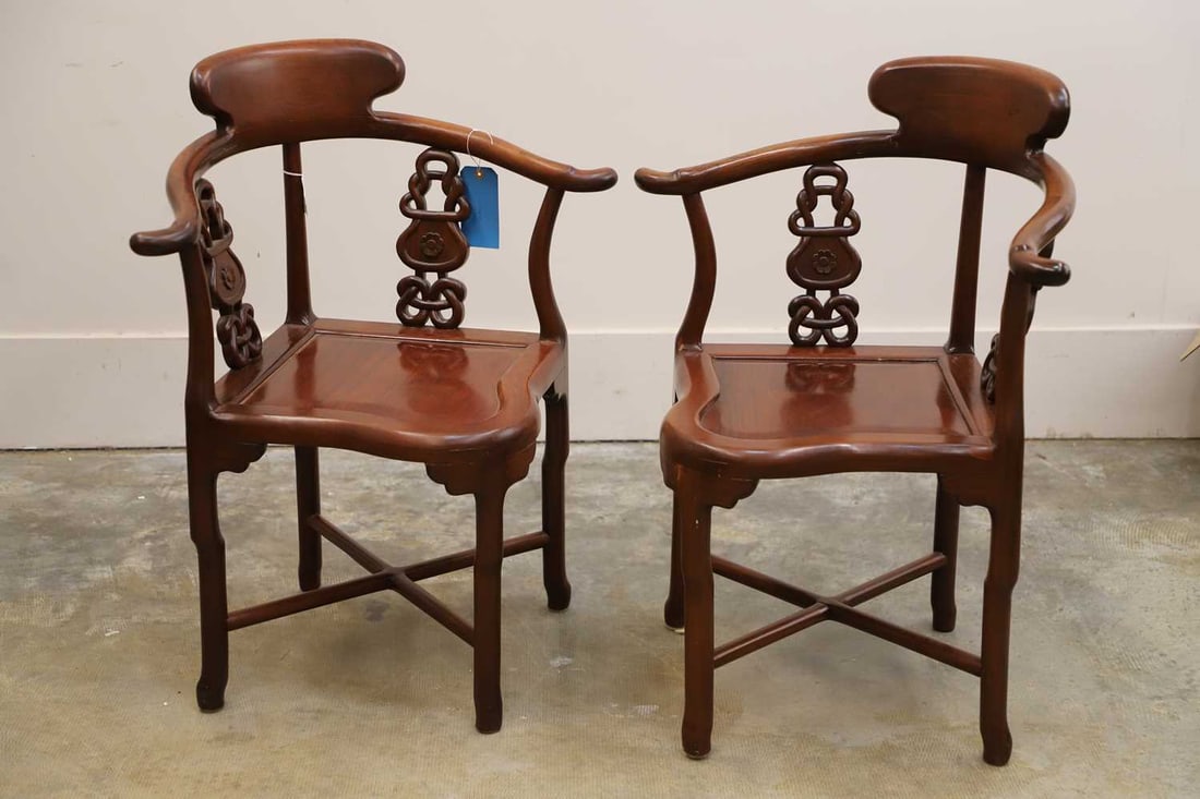 A pair of Chinese hardwood horseshoe back corner chairs, 20th century,: A pair of Chinese hardwood horseshoe back corner chairs, 20th century, each with a curved crest rail continuing into outscrolled arms, supported by shaped and pierced splats, carved with stylised orn