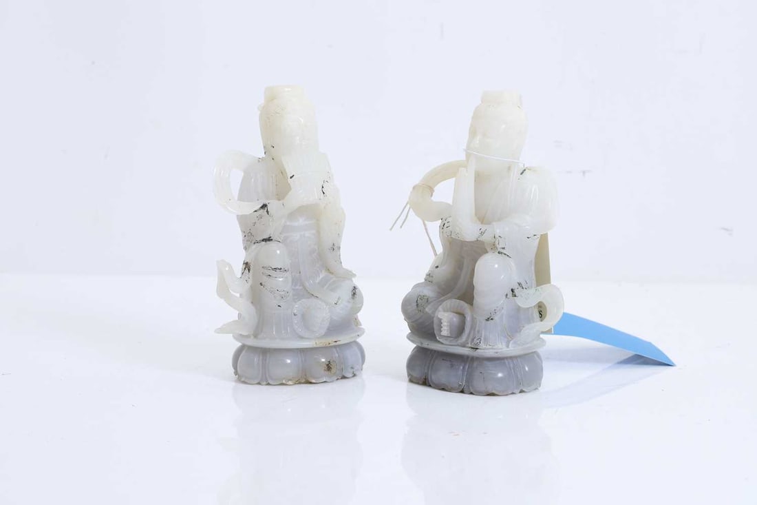 A pair of Chinese jade Daoist figures, 20th century,: A pair of Chinese jade Daoist figures, 20th century, each modelled seated playing a Yu instrument, wearing flowing robes on lotus carved bases 15.5cm high 2 Condition Report: Some staining and
