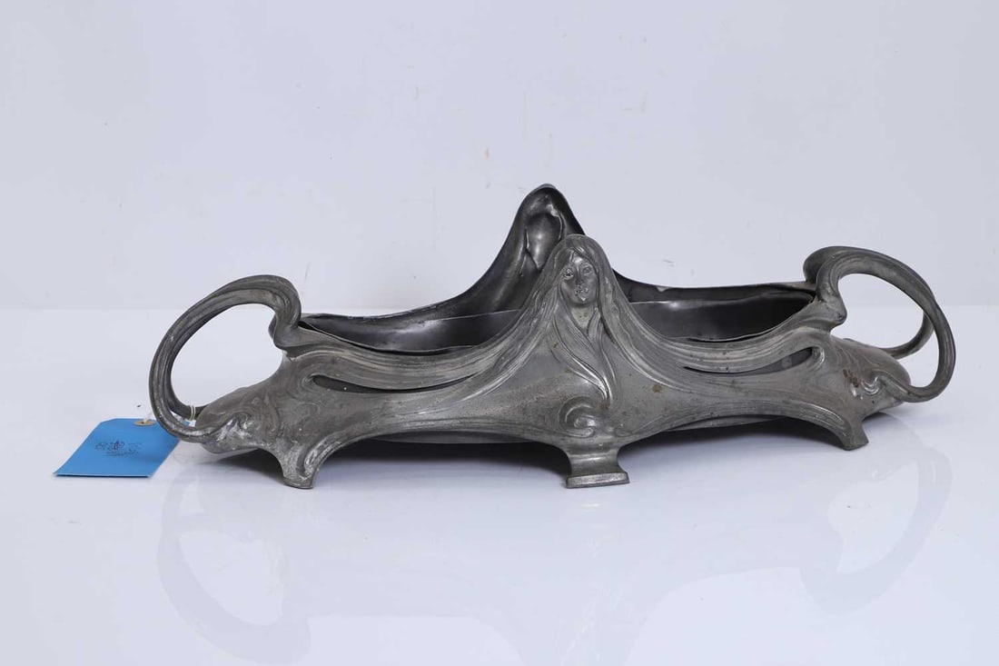 An Art Nouveau pewter centrepiece, 20th century,: An Art Nouveau pewter centrepiece, 20th century, of oval form, with looped handles to either end and centered by a mask 54cm wide, 15.5cm high