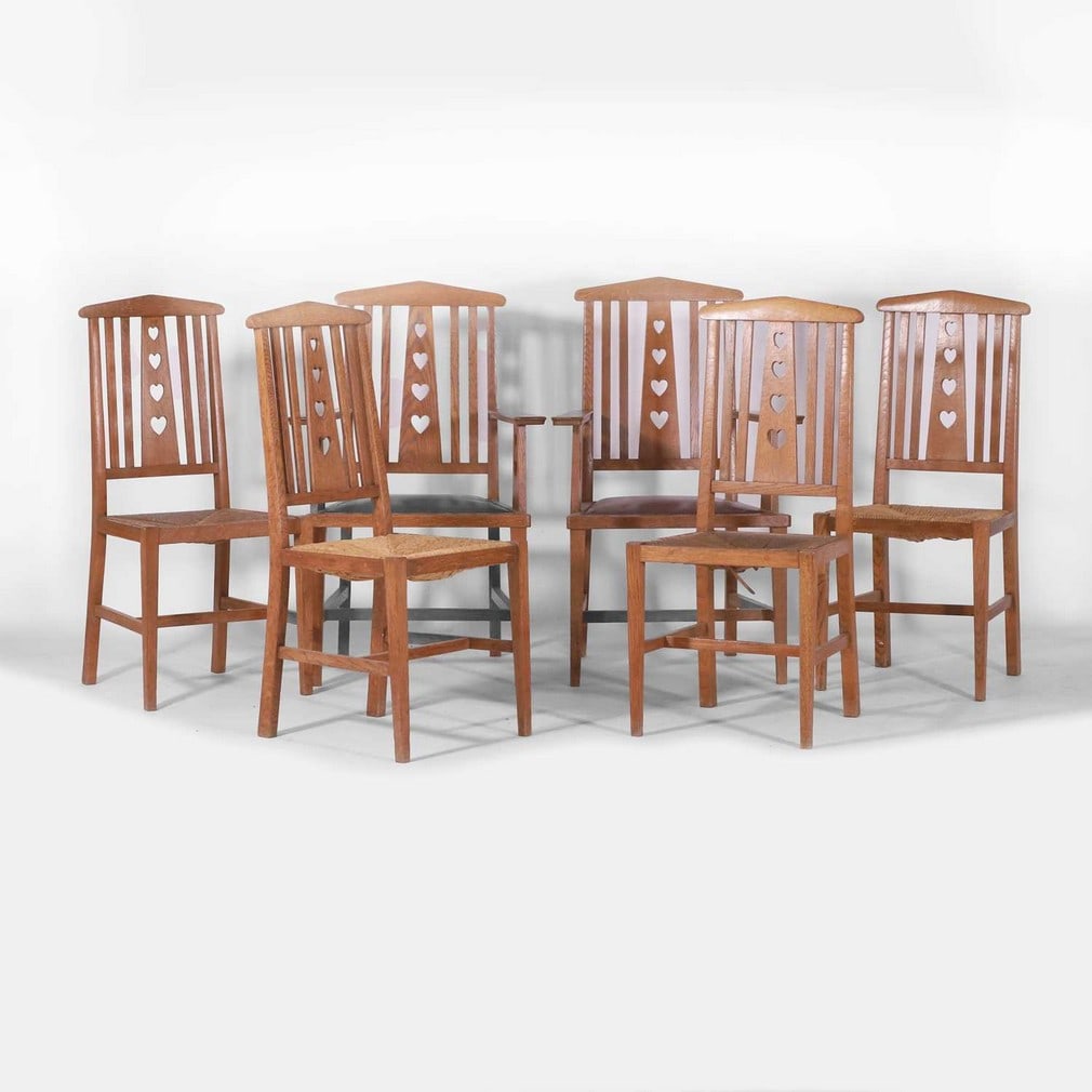 Arts and Crafts, a set of six chairs,: Arts and Crafts, a set of six chairs, circa 1940s, comprising two carvers and four dining chairs, each oak frame with pierced heart cut-out decoration over a rush seat, the two carvers with leather se