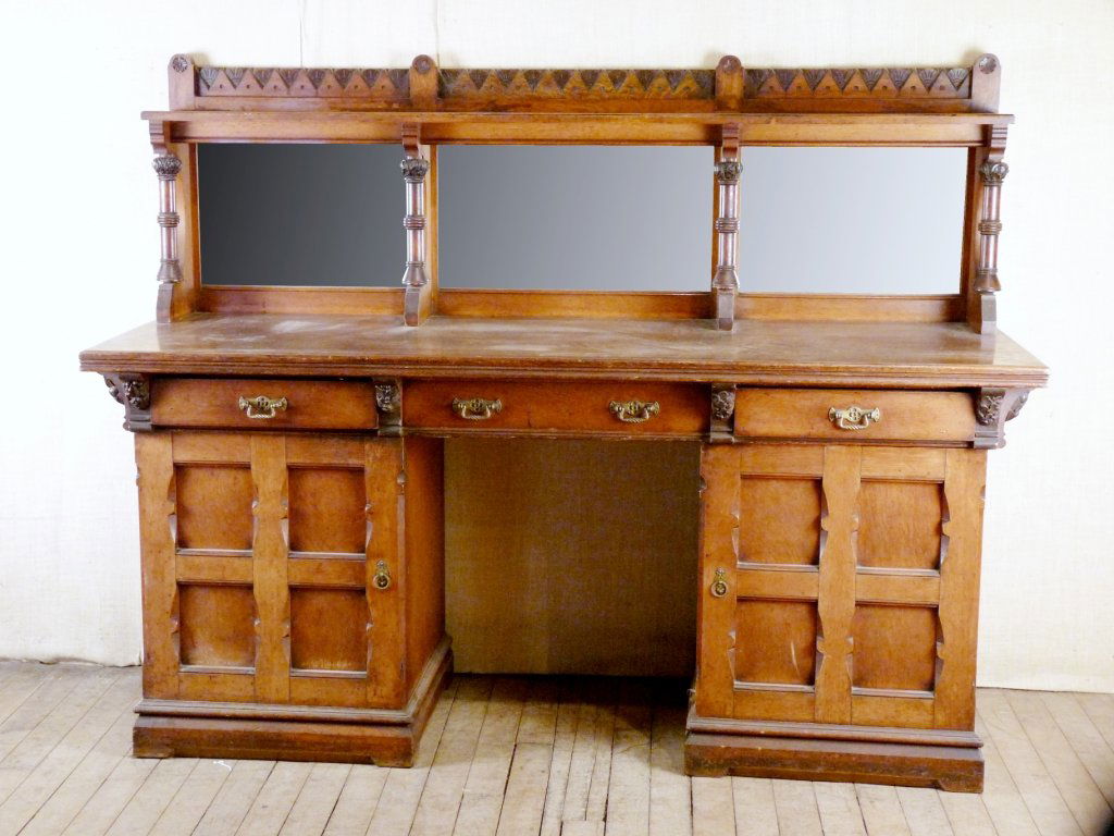 An Aesthetic oak sideboard, the back with a shelf on fo: An Aesthetic oak sideboard, the back with a shelf on four columns, and three mirror panels over three drawers and an open centre, flanked by a pair of cupboards, 199cm wide 70cm deep 156cm high