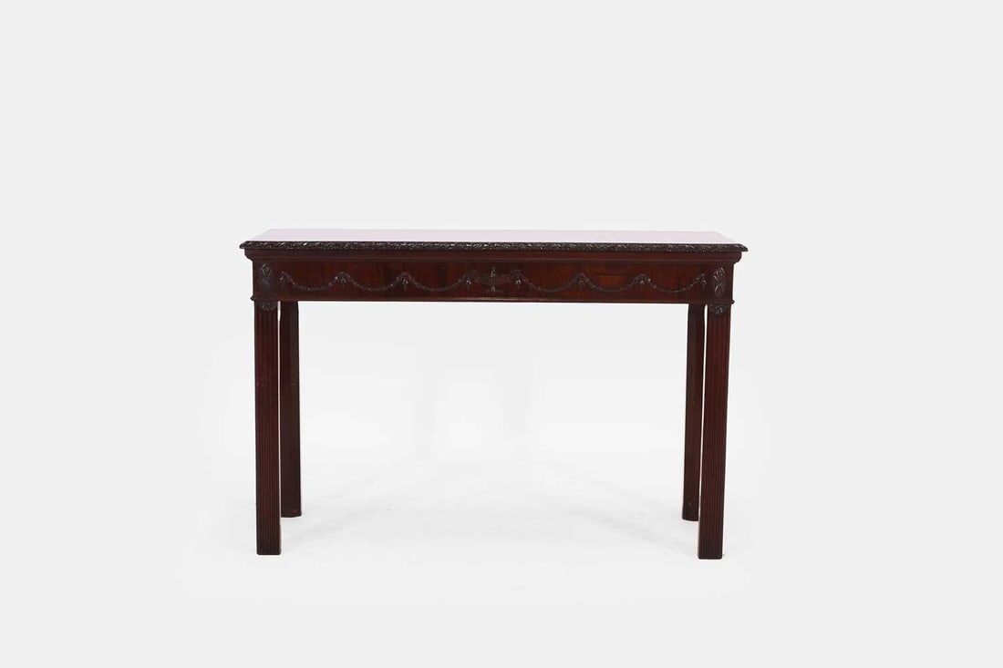 A George III-style mahogany side table, c.1880,: A George III-style mahogany side table, c.1880, the plain rectangular top with a carved edge, the frieze with swags and paterae, raised on fluted square supports. 12.5cm wide, 59cm deep, 77.5cm highC