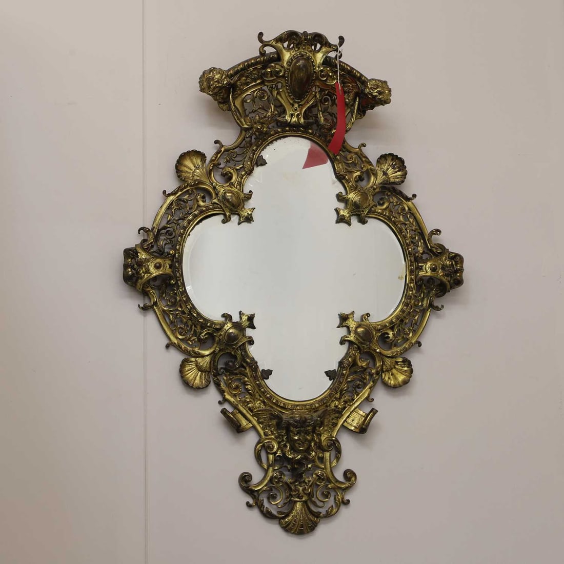 A Victorian gilt-metal mirror, 20th century,: A Victorian gilt-metal mirror, 20th century, with a scrolling foliate frame decorated with masks, around a shaped mirror plate 60cm wide, 85cm high Condition Report: Some flaking and peeling to