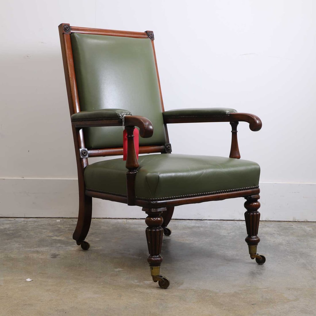 A William IV mahogany framed library chair,: A William IV mahogany framed library chair, the rectangular padded back with corner roundels, the back, arms and seat upholstered in green leather, raised on turned tapering and reeded front legs