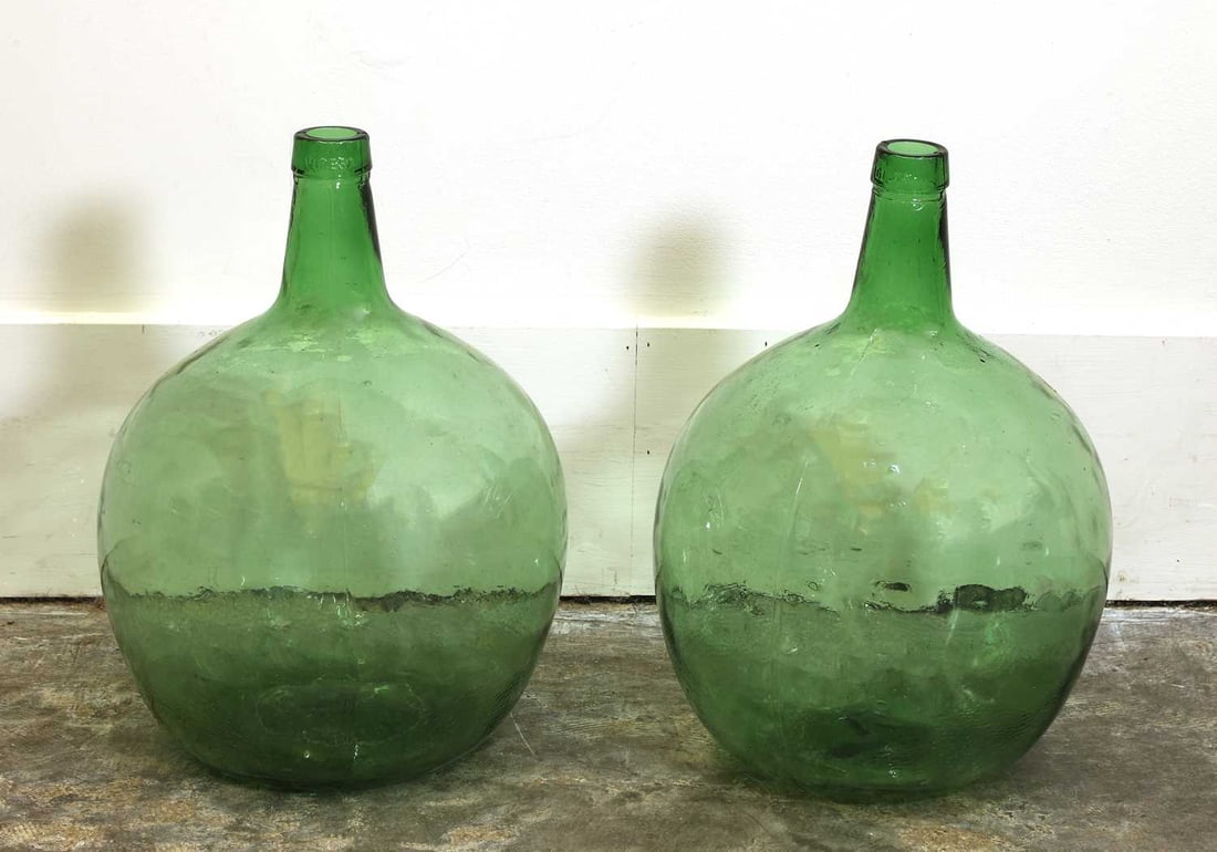 A pair of green Glass Demijohns,: A pair of green Glass Demijohns, of baluster form, with a embossed and moulded spout, 31cm wide 43cm high each 2 Provenance: from a provincial french estate