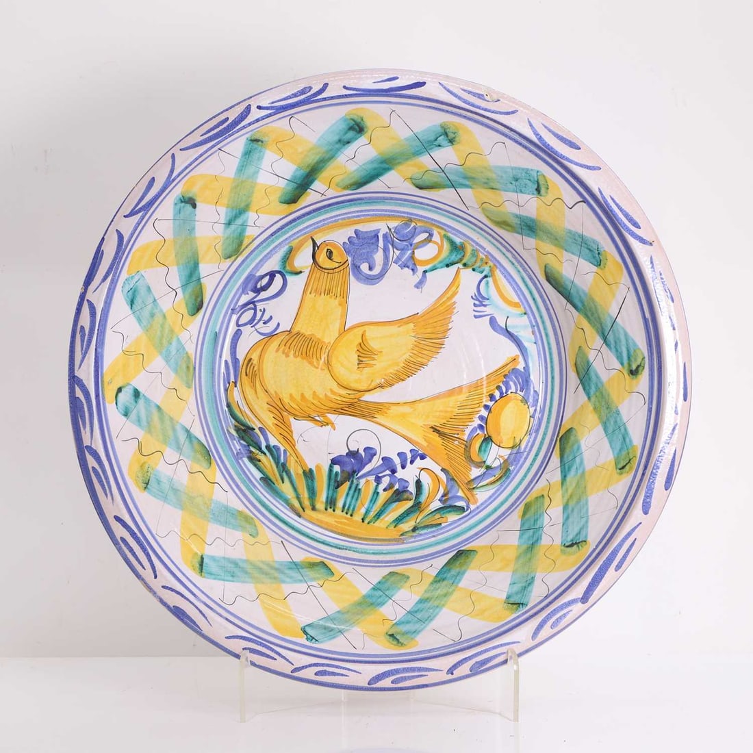 A large tin-glazed earthenware 'lebrillo' basin, 19th century, Spanish,: A large tin-glazed earthenware 'lebrillo' basin, 19th century, Spanish, decorated in greens, blues and yellows with a yellow bird to the centre, the rim with criss-cross line work 56.5cm wide, 16cm hi