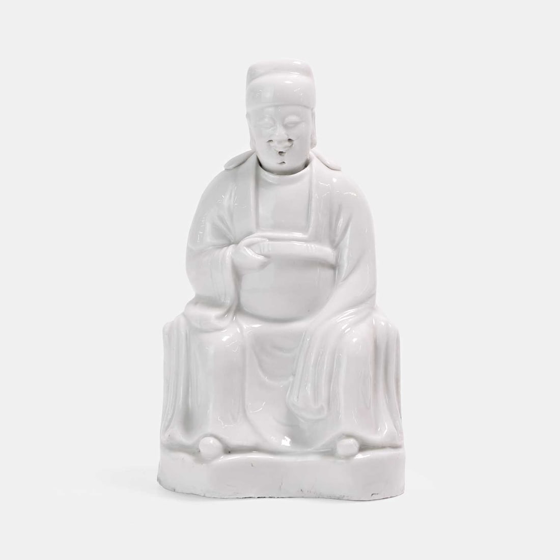 A Dehua blanc de chine seated figure of Wenchang,: A Dehua blanc de chine seated figure of Wenchang, seated on a raised plinth, wearing scholar robes, and holding a belt in his hand 10cm wide, 17cm high
