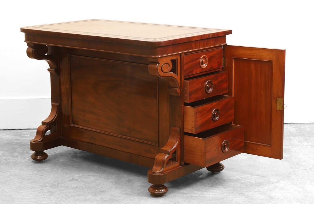 A Victorian library table, early 20th century,: A Victorian library table, early 20th century, the tooled leather writing surface above a pair of opposing cupboards to scrolling front pillars, each cupboard encasing an arrangement of drawers, base