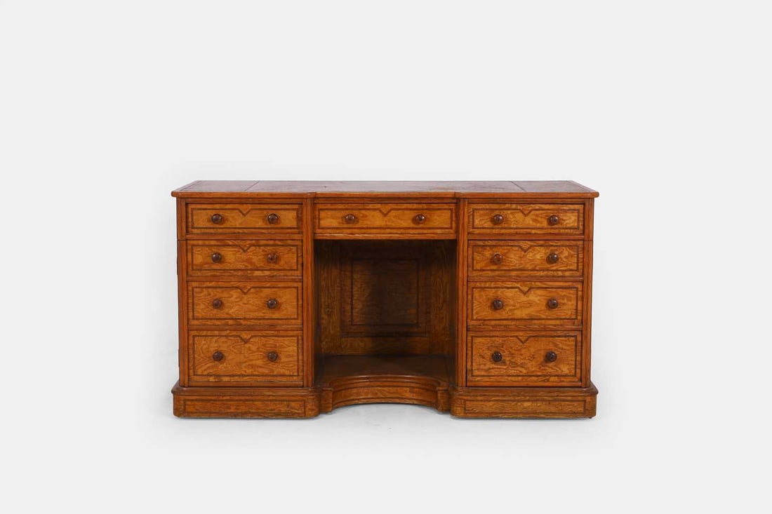 A Hungarian ash kneehole desk, second half of the 19th century,: A Hungarian ash kneehole desk, second half of the 19th century, of inverted breakfront outline with a gilt-tooled leather top, above a frieze drawer and two pedestals fitted with cupboards, raised on