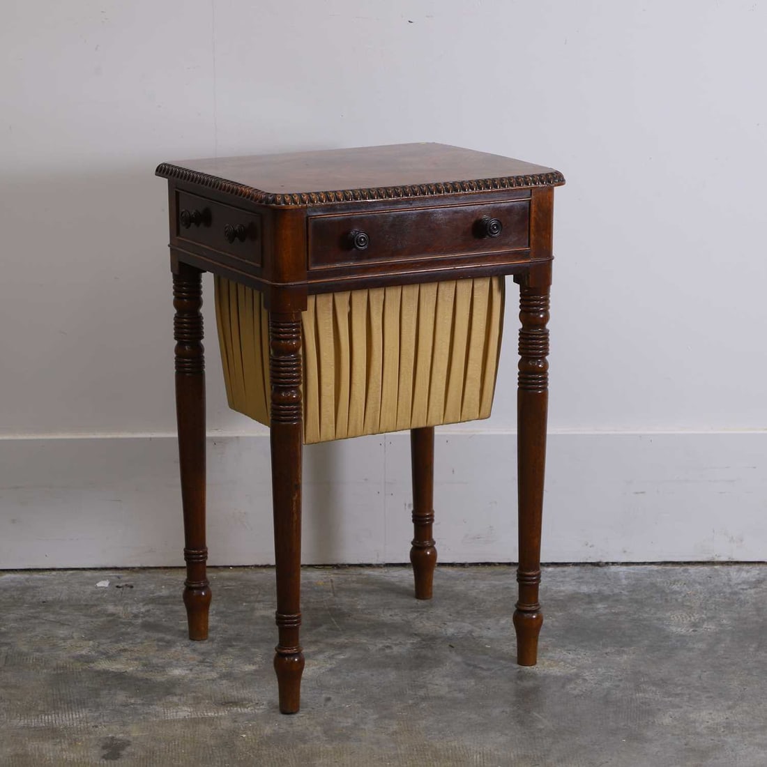 A Regency mahogany work table, 19th century,: A Regency mahogany work table, 19th century, the rounded rectangular top with a beaded moulding, over a frieze drawer and a pleated silk sliding well, on turned tapering supports 44.5cm wide, 38cm