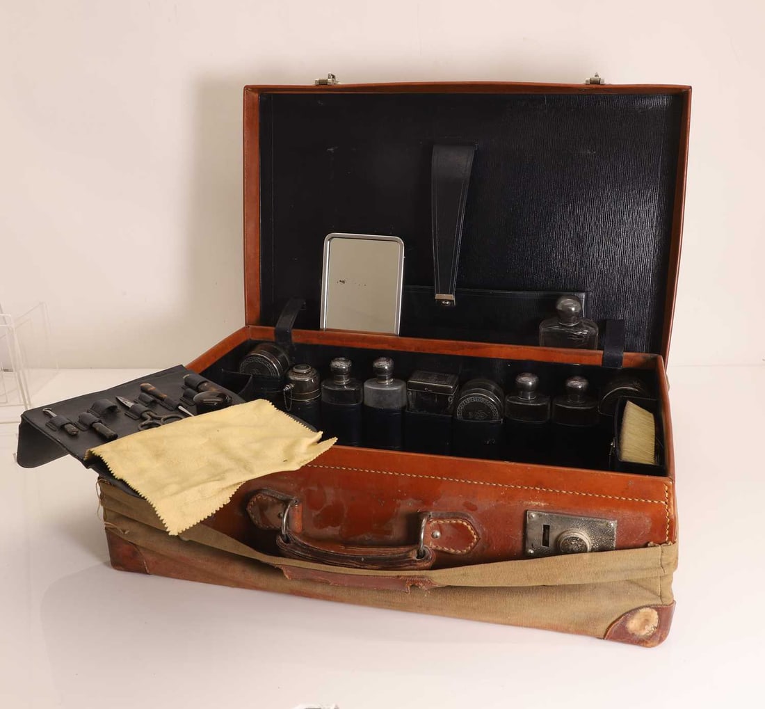 A leather vanity case with silver mounted items,: A leather vanity case with silver mounted items, to include etched glass bottles and canisters with silver-mounted covers, most with crowned crest, together with a leather-bound blotting book, and a t