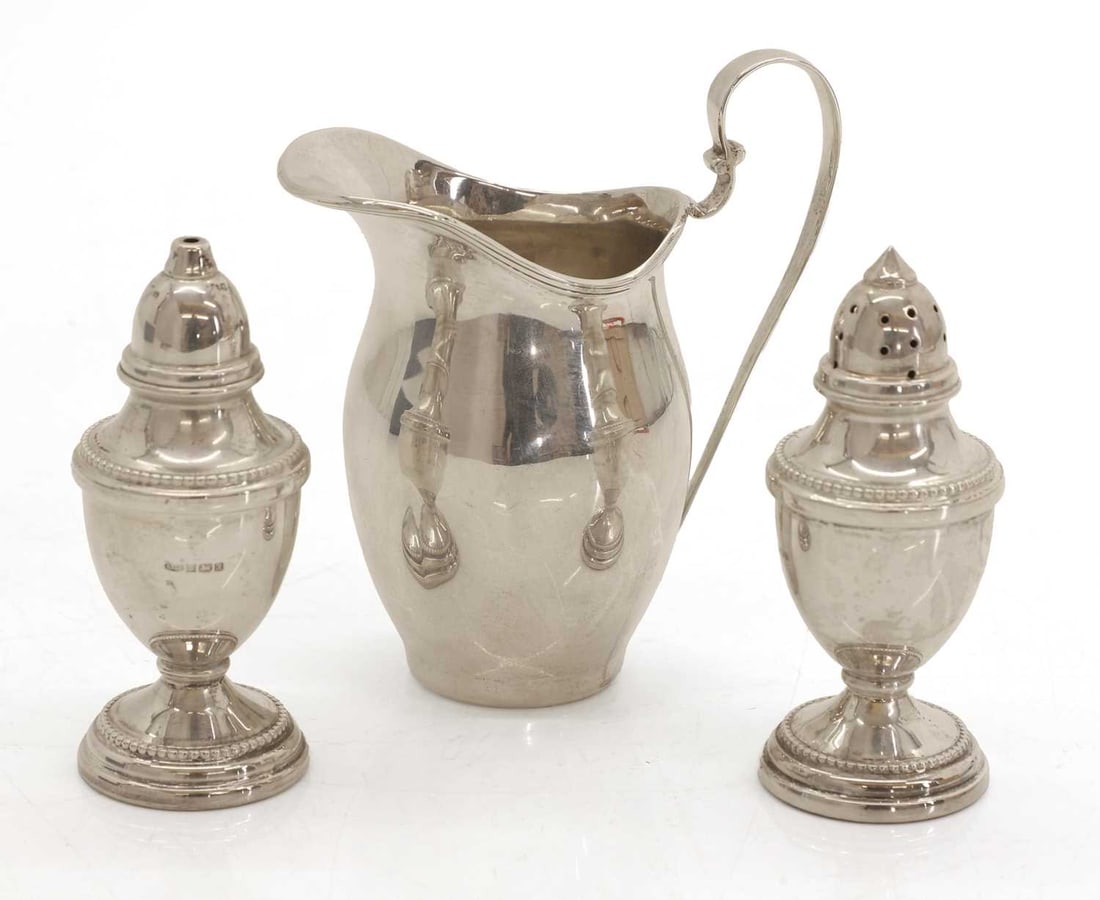 A collection of three silver table items,: A collection of three silver table items, to include an Asprey helmet jug, London, 1919, together with a pair of pepperettes, by W I Broadway & Co, Birmingham, 1994, with beaded decoration, filled