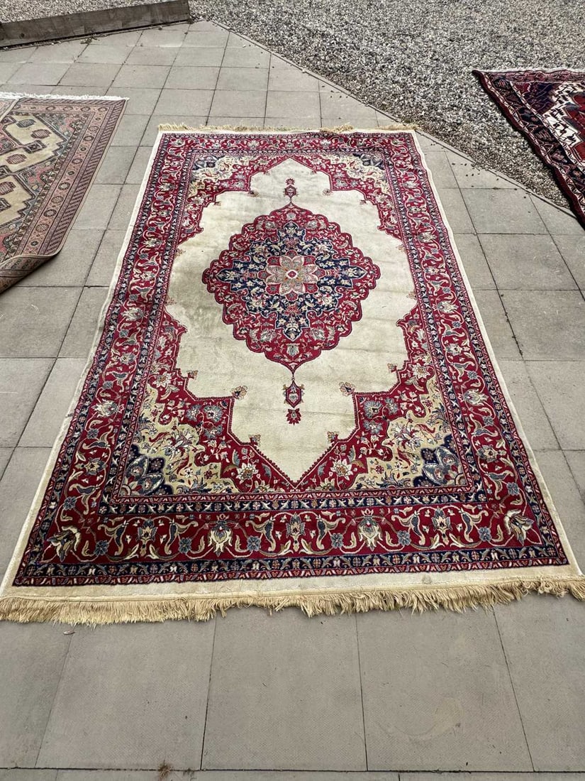 A Kashmiri carpet, 20th century,: A Kashmiri carpet, 20th century, the ivory field centred by a lobed medallion issuing stylised pendants, to a red boarder of scrolling foliate decoration 195 x 305cm Condition Report: Some wear and