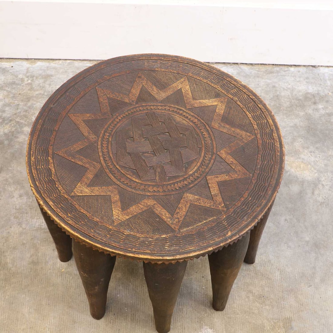A carved hardwood Nupe stool, 20th century, Nigeria,: A carved hardwood Nupe stool, 20th century, Nigeria, the circular top deeply carved with concentric geometric bands centred by an interlaced knot motif within a radiating star design, the edge with fu