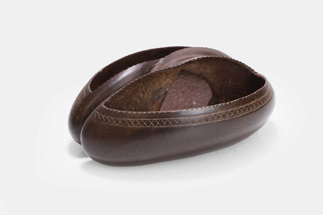 A coco de mer nut basket,: A coco de mer nut basket, the natural form hollowed and shaped as an open vessel, the exterior carved with a band of geometric ornament 33cm wide, 16cm high