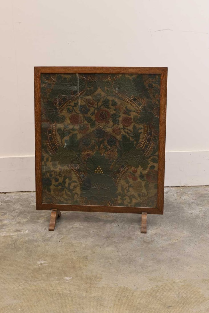 An Arts & Crafts embossed, polychrome, and gilt leather panel, late 19th century, in the manner of W: An Arts & Crafts embossed, polychrome, and gilt leather panel, late 19th century, in the manner of William Morris, depicting scrolling leaves and pomegranates, fitted within a later oak glazed firescr