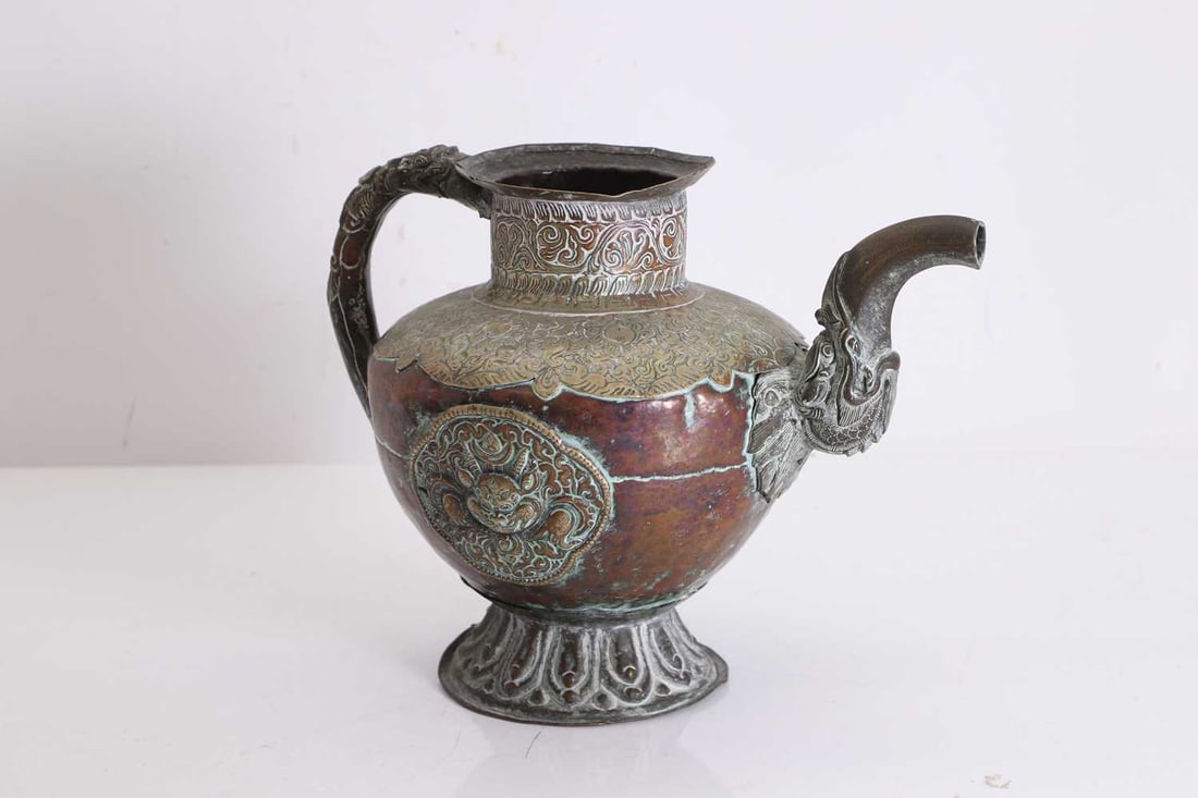 A Tibetan brass teapot, 20th century,: A Tibetan brass teapot, 20th century, the body decorated with brass panels of mythical beasts, the shoulders with a brass plate of dense scrolling foliage, the handle and spout modelled as a stylised