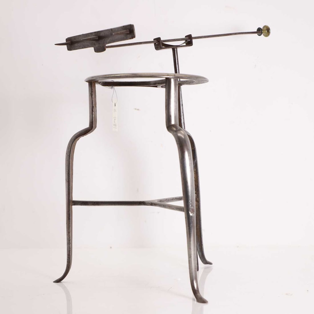 A steel trivet, 19th century: A steel trivet, 19th century the stand of tripod form with circular trivet to the top and shaped legs joined by stretchers, surmounted by a spit, with turned brass terminal, the adjustable cradle supp