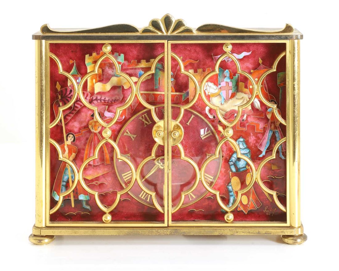 An Imhof enamel and gilt metal table clock, mid 20th century,: An Imhof enamel and gilt metal table clock, mid 20th century, the case with hinged pierced lattice doors opening to reveal an enamelled scene of knights, attendants, and battlements surrounding a Roma