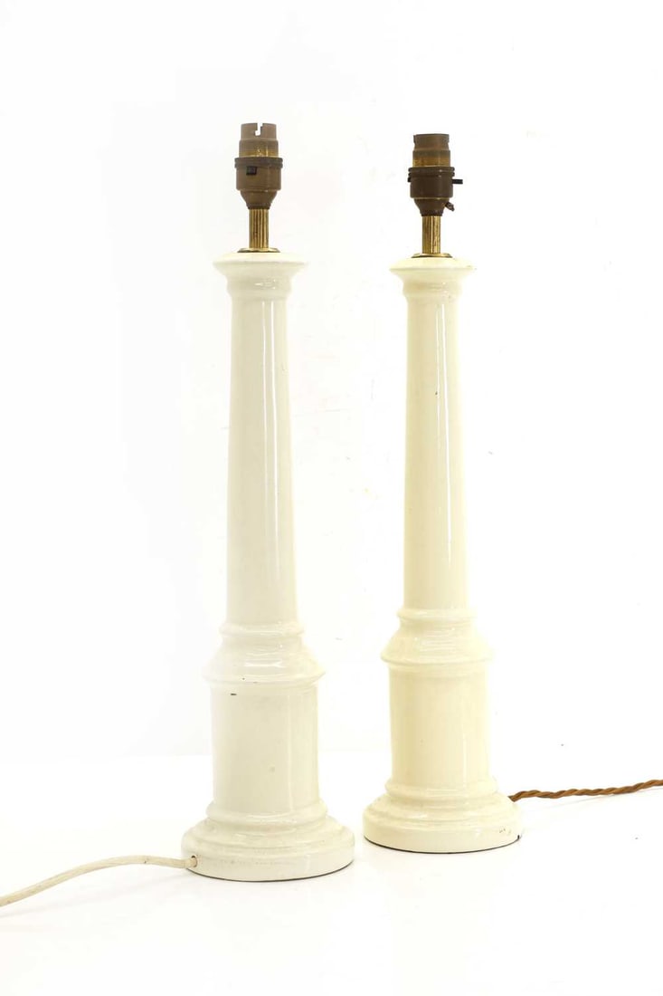 A pair of ceramic column table lamps, 20th century,: A pair of ceramic column table lamps, 20th century, each of tapering cylindrical form with moulded socle and stepped bases, glazed in off-white, fitted with brass bulb holders 11.5cm wide, 49cm high 2