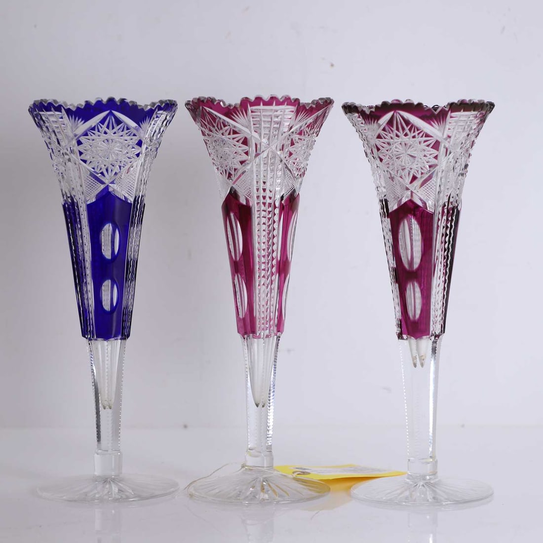 Three Bohemian ruby and blue cased glass vases, 20th century and later,: Three Bohemian ruby and blue cased glass vases, 20th century and later, Czech or Belgian, each of flared form with scalloped rim, deeply cut with hobstar centres, diamond panels and facet cuts, cased