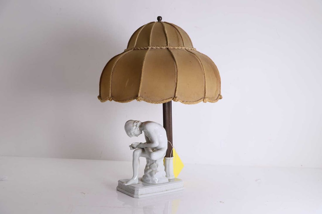 A Vienna porcelain table lamp, late 19th to early 20th century: A Vienna porcelain table lamp, late 19th to early 20th century modelled as Spinario, beside a fluted brass column below a braided shade, underglaze shield mark 47cm high including shade