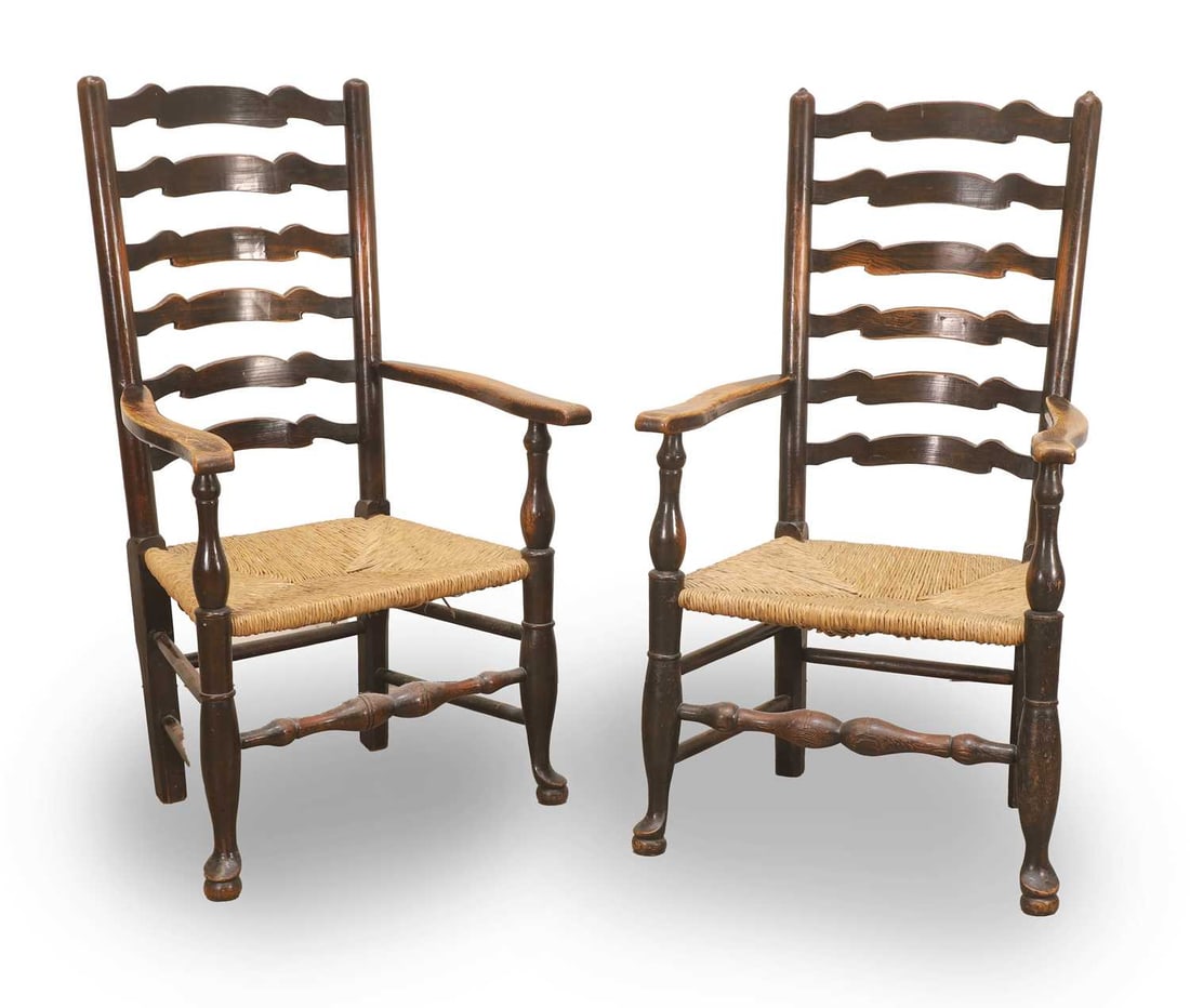 Two Lancashire oak ladderback elbow armchairs, 19th century,: Two Lancashire oak ladderback elbow armchairs, 19th century, each with six shaped splats above a rush seat, raised on turned supports united by stretchers, with pad feet 60cm wide, 50cm deep, 101cm