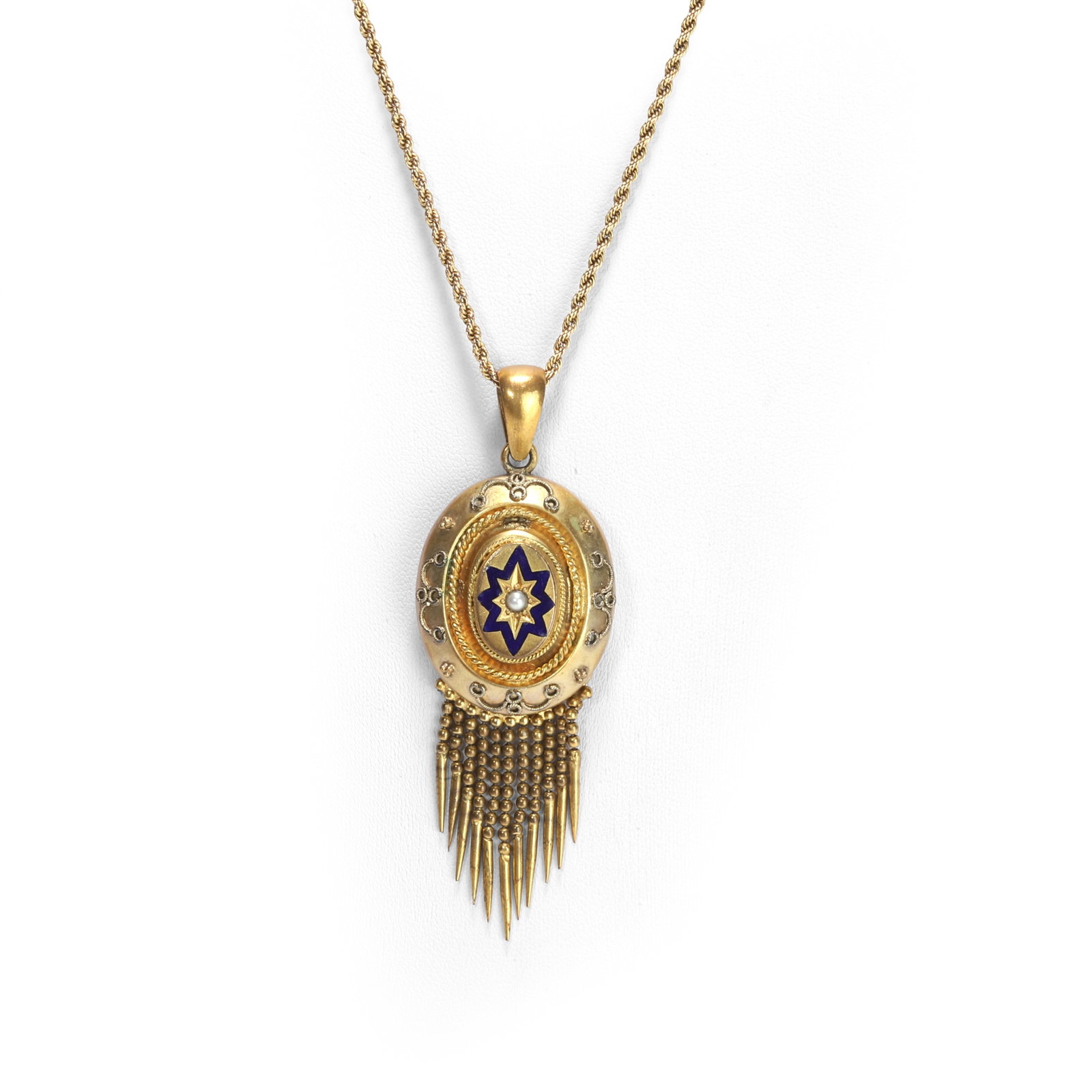 A Victorian archaeological revival tassel pendant on chain,: A Victorian archaeological revival tassel pendant on chain, the pendant of oval form with a central seed pearl star set and a blue enamel star surround, the outer layers decorated with rope borders an