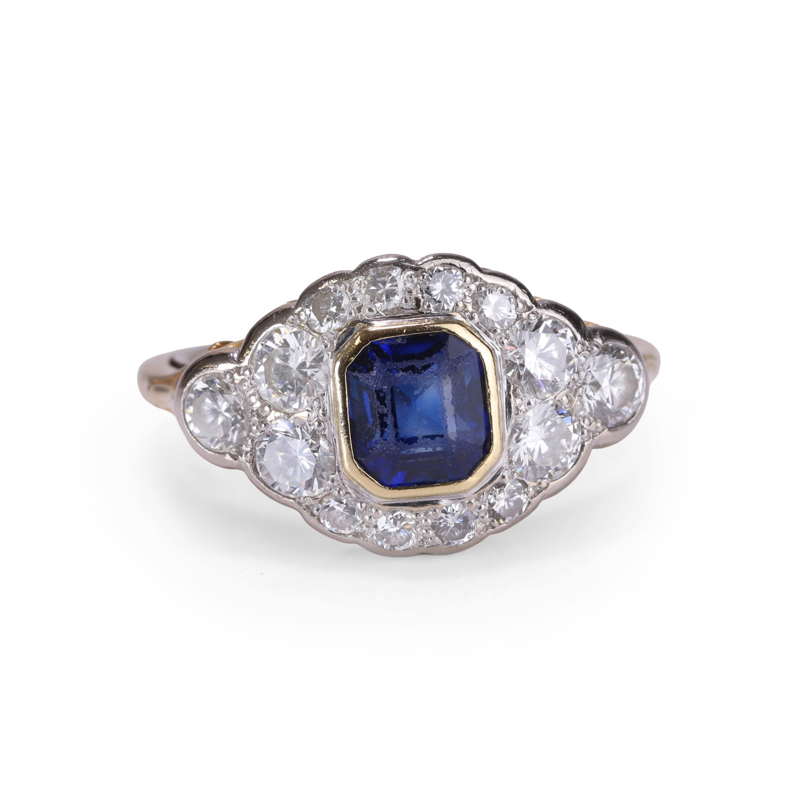 A sapphire and diamond cluster ring,: A sapphire and diamond cluster ring, centred with a cushion shape sapphire within a surround of graduated round brilliant cut diamonds, the diamonds grain set in white upon a yellow gold pierced galle