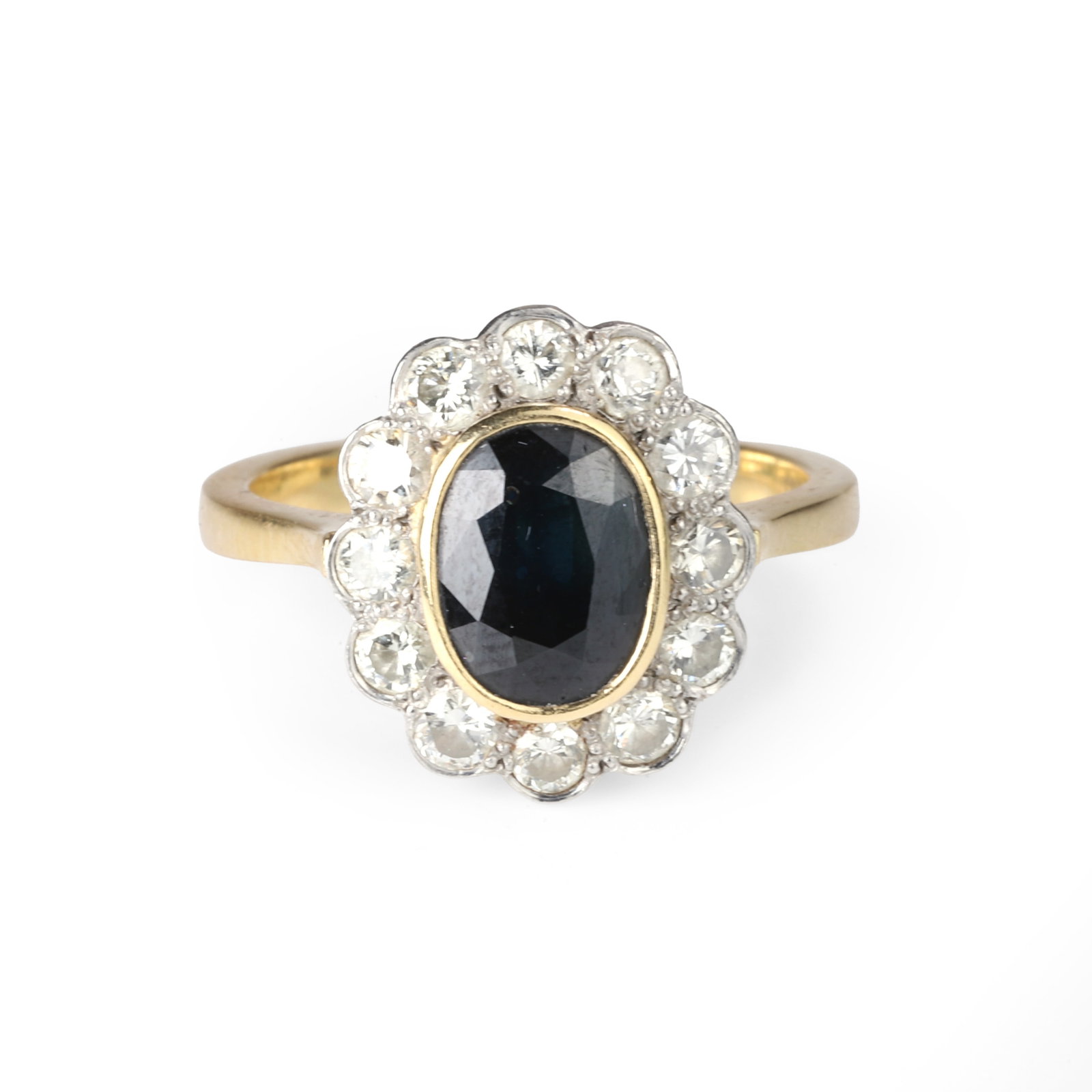 An 18ct gold sapphire and diamond cluster ring,: An 18ct gold sapphire and diamond cluster ring, comprising an oval cut sapphire, rub over set in yellow gold and surrounded by twelve round brilliant cut diamonds, thread and scallop set to a tapered 