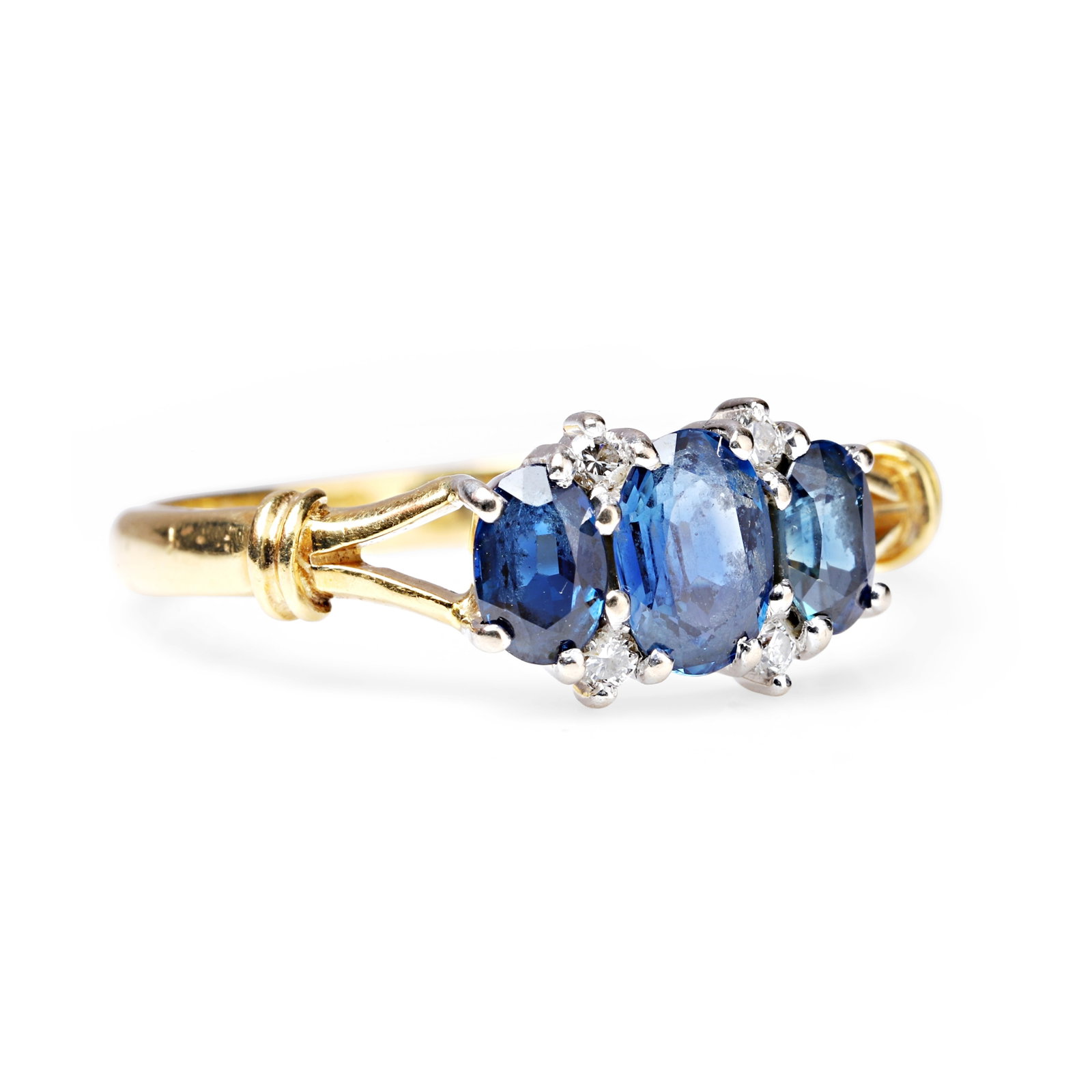 Cropp & Farr, an 18ct gold sapphire three stone ring,: Cropp & Farr, an 18ct gold sapphire three stone ring, featuring three graduated oval cut sapphires spaced with small round brilliant diamond accents, all claw set between bifurcated shoulders. Maker's