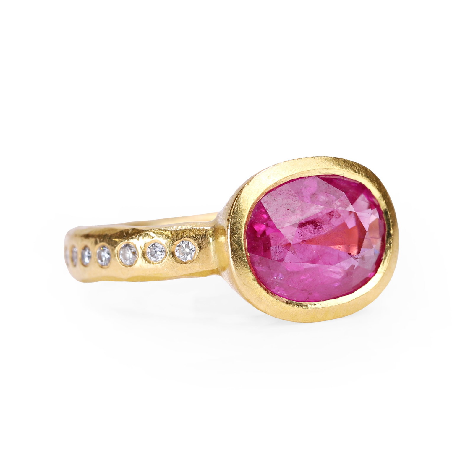 Malcolm Betts, a 22ct gold ruby and diamond ring,: Malcolm Betts, a 22ct gold ruby and diamond ring, the oval cut pinkish ruby horizontally set in a plain bezel, flanked by lines of round brilliant cut diamonds, into a hammered finish hoop. Hallmarked