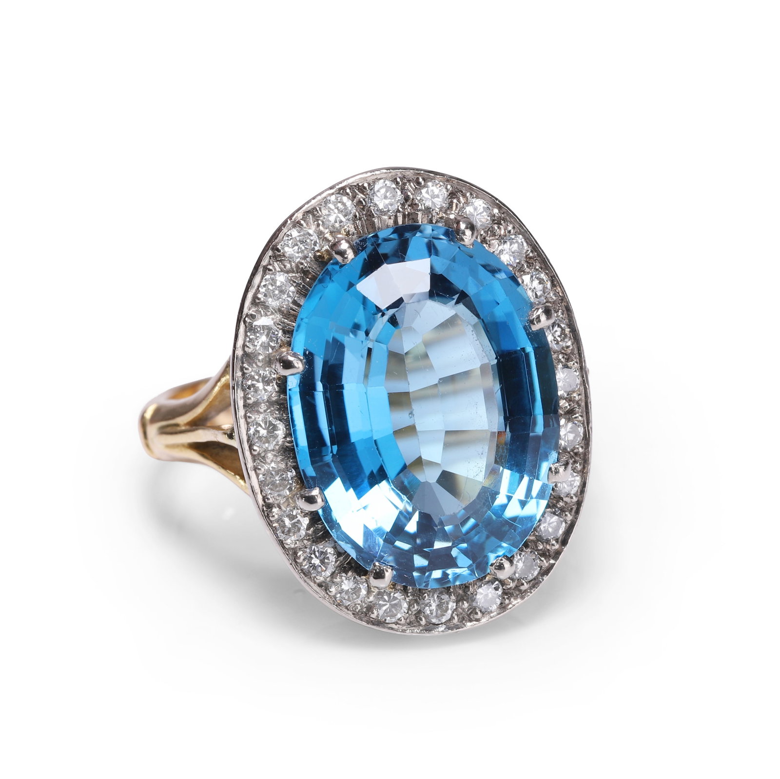 A blue topaz and diamond cluster ring,: A blue topaz and diamond cluster ring, the central oval mixed cut blue topaz claw set with a halo of round brilliant cut diamonds, to a galleried mount and split shoulder with straight band and sizing