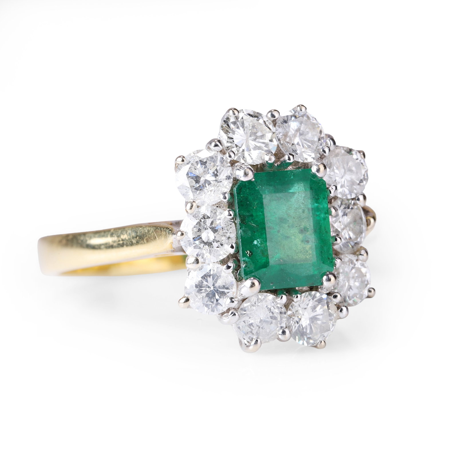 An 18ct gold emerald and diamond cluster ring,: An 18ct gold emerald and diamond cluster ring, the emerald cut emerald set with four white gold corner claws and surrounded by ten claw set round brilliant cut diamonds to a tapered gold band. Hallmar