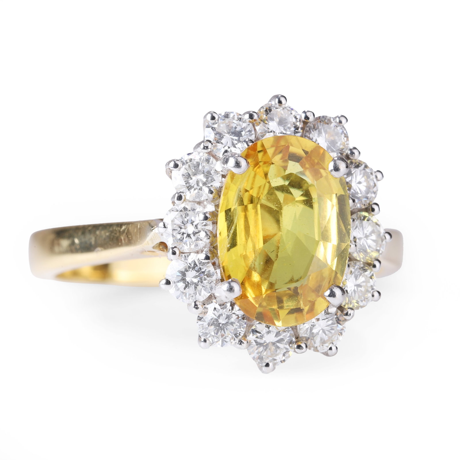 An 18ct gold yellow sapphire and diamond ring,: An 18ct gold yellow sapphire and diamond ring, the oval mixed cut yellow sapphire estimated to weigh 2.20ct, encircled by a surround of brilliant-cut diamonds, all claw set in white to a yellow gold