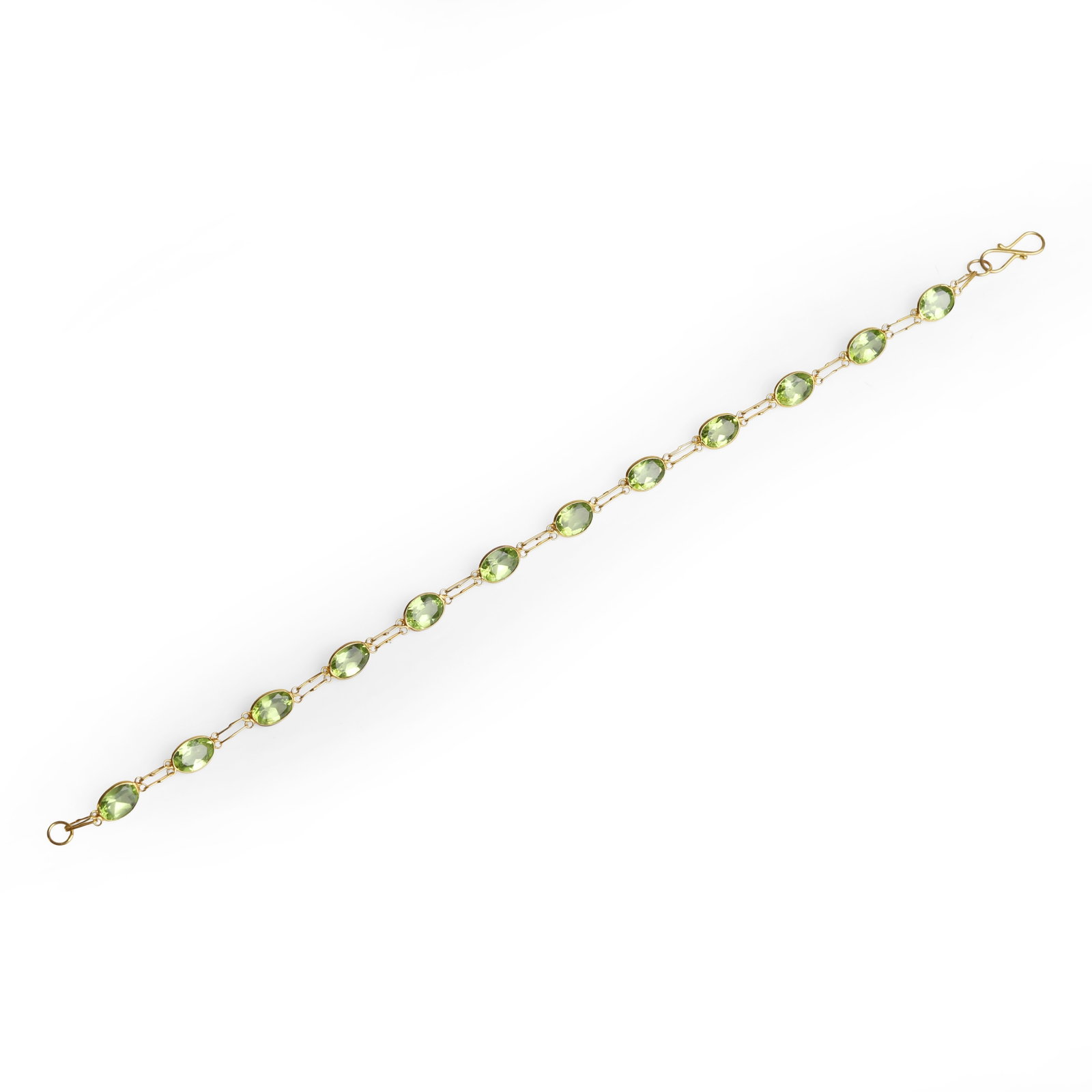 A peridot set line bracelet,: A peridot set line bracelet, spectacle set with a single line of oval cut peridots, each alternating to doubled fetter links, to an 'S' shaped clasp, tested as approximately 14ct gold (Length 19cm; 2.