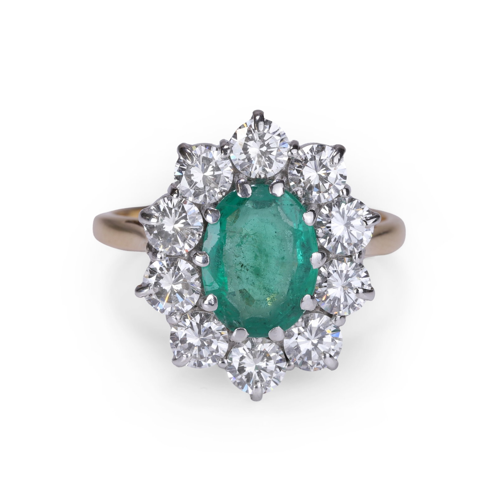 An 18ct gold emerald and diamond cluster ring,: An 18ct gold emerald and diamond cluster ring, the oval mixed cut emerald claw set within a surround of round brilliant cut diamonds, between chenier shoulders into a plain hoop. Partially hallmarked 