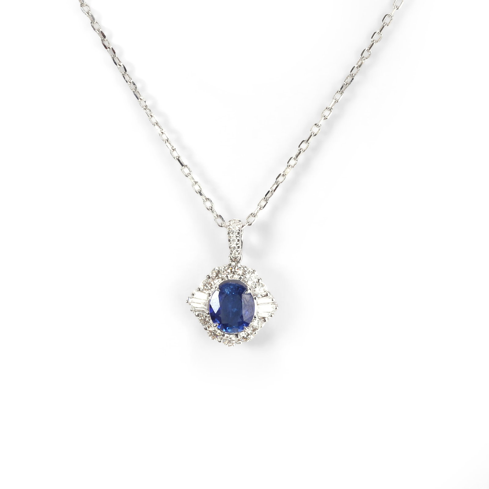 A sapphire and diamond pendant necklace,: A sapphire and diamond pendant necklace, the oval cut sapphire within a round brilliant cut diamond and tapered baguette 'ballerina' surround, suspended on a trace link chain, stamped 750, surface tes
