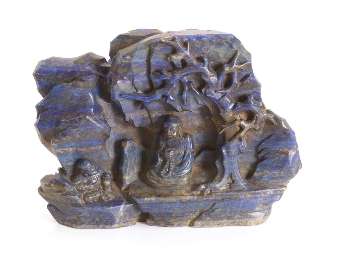 A Chinese carved lapis lazuli group, 20th century,: A Chinese carved lapis lazuli group, 20th century, depicting a luohan seated under a tree in a rocky landscape, beside a young boy 19cm wide