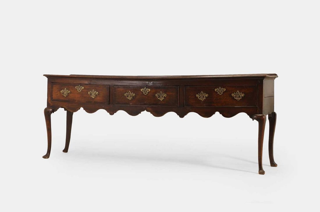 A George II oak dresser, mid-18th century,: A George II oak dresser, mid-18th century, with a moulded rectangular top, above three crossbanded drawers set with chinoiserie brass handles, with a wavy apron, raised on cabriole supports (231cm wid