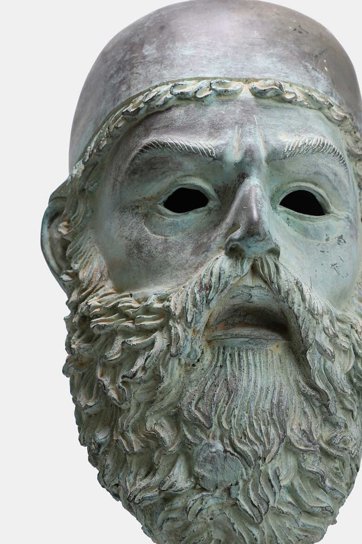 A patinated bronze mask of a Riace Warrior, of recent manufacture,: A patinated bronze mask of a Riace Warrior, of recent manufacture, mounted on a pink marble stepped base (21cm wide, 27cm deep, 55cm high) Condition Report: Signifcant patination throughout. Some disc