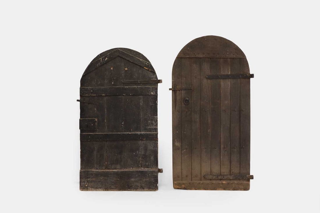 Two large iron-bound oak doors, 19th century,: Two large iron-bound oak doors, 19th century, both of arched rectangular outline, with fitted latches, the shorter example with the handle side painted in white (smaller door 109cm wide, 9cm deep, 187