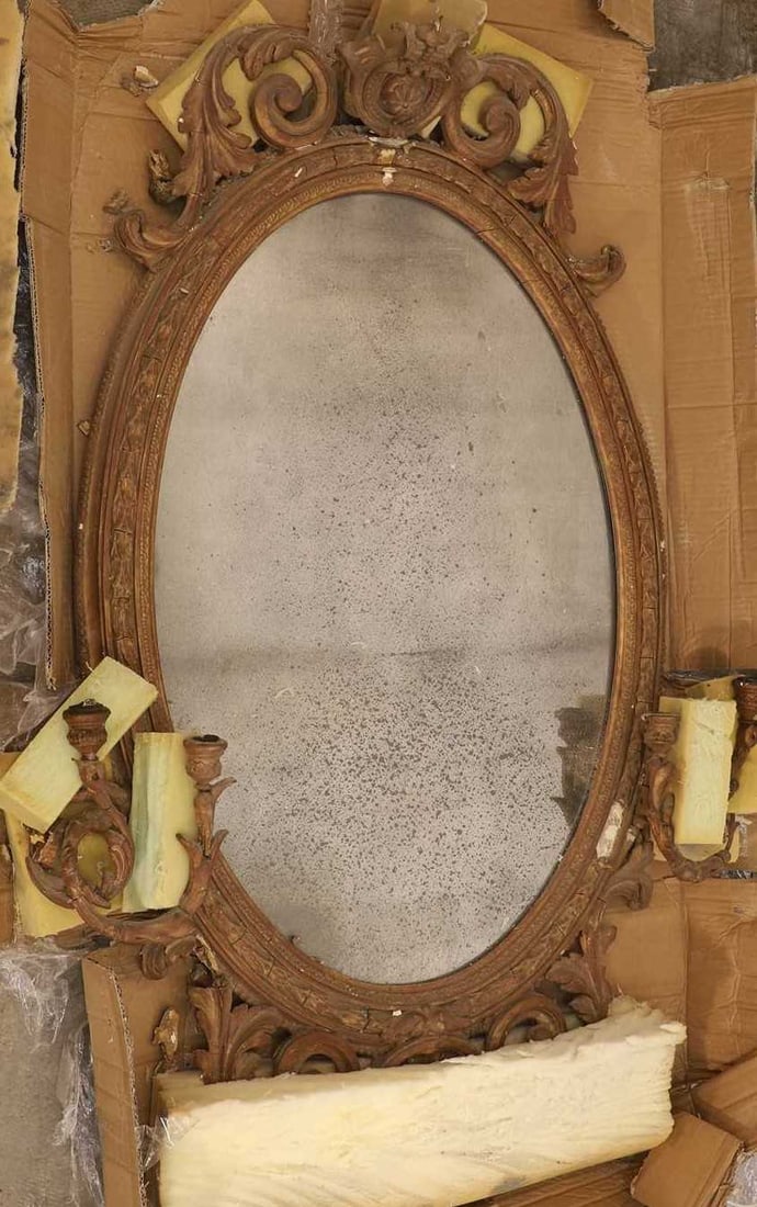 An oval giltwood and gesso mirror,: An oval giltwood and gesso mirror, with scrolling supports and a pair of opposing candle holders to each side 83cm wide, 125cm high