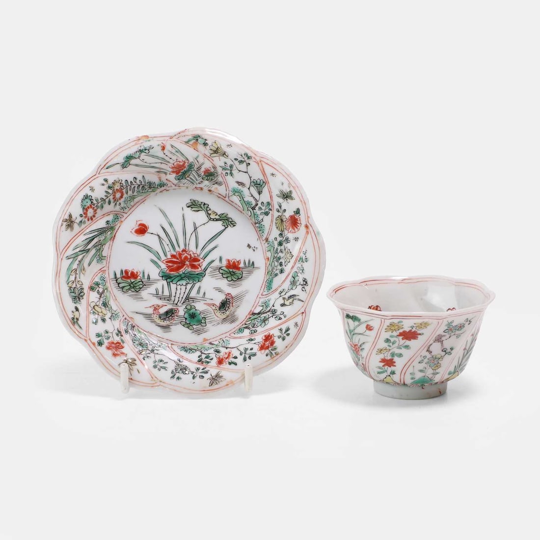 A Chinese wucai teacup and saucer, Kangxi (1662-1722),: A Chinese wucai teacup and saucer, Kangxi (1662-1722), of lobed form, the saucer painted with Mandarin ducks in a lotus pond to the centre, enclosed with a border of birds and flowers in spiral-fluted